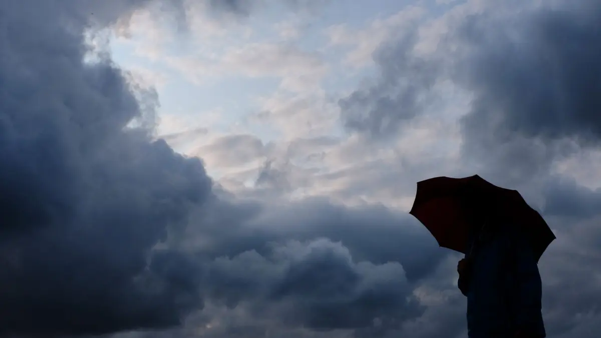 Wolken und Regen in Hessen: ARCHIV - 12.07.2019, Nordrhein-Westfalen, Duisburg: Ein Mann geht mit einem Regenschirm vor aufziehenden dunklen Wolken spazieren. (Symbolbild) (zu dpa: «Im Norden heiter, im Süden regnerisch») Foto: Martin Gerten/dpa +++ dpa-Bildfunk +++