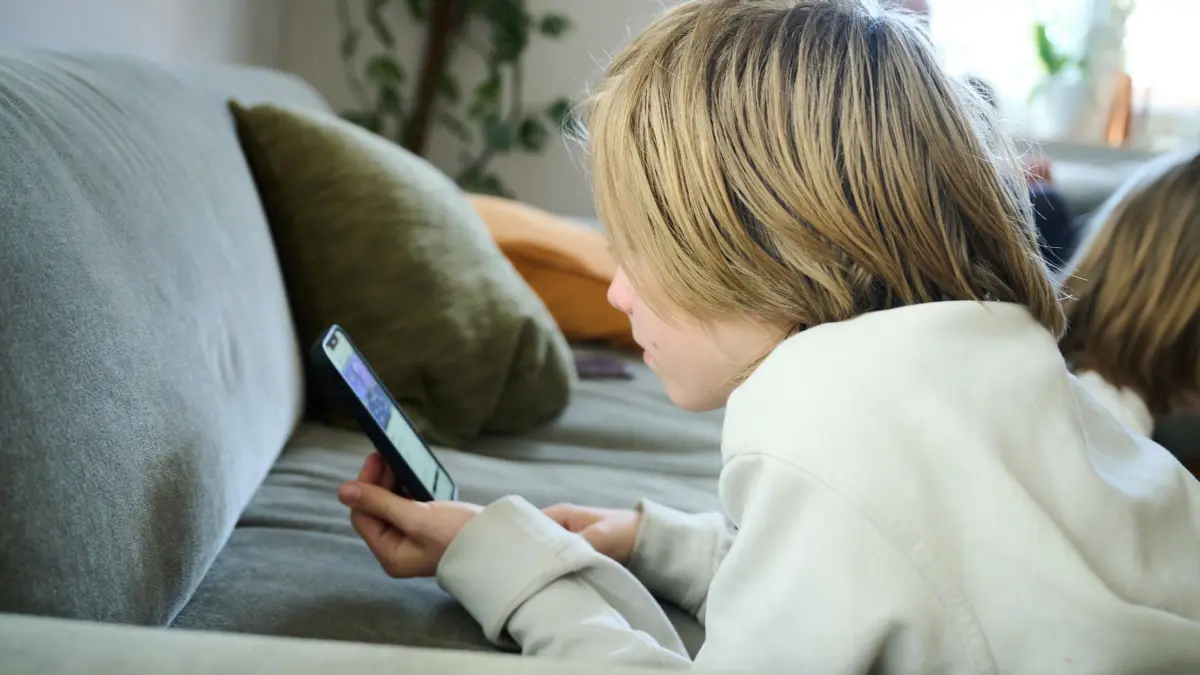 Symbolbild - Smartphone-Nutzung bei Kindern: ARCHIV - 21.04.2025, Bayern, Roth: ILLUSTRATION - Ein Junge liegt auf einem Sofa und guckt auf sein Smartphone. (gestellte Szene). Kinder und Jugendliche verbringen immer früher immer mehr Zeit am Bildschirm - sei es für Tiktok, Online-Spiele oder zum Lernen.
Ein Junge scrollt an seinem Handy. Fachleute fordern strengere Regeln für Kinder, die im Internet unterwegs sind. (zu dpa: «Social Media: Länder fordern mehr Schutz für Kinder») Foto: Annette Riedl/dpa +++ dpa-Bildfunk +++