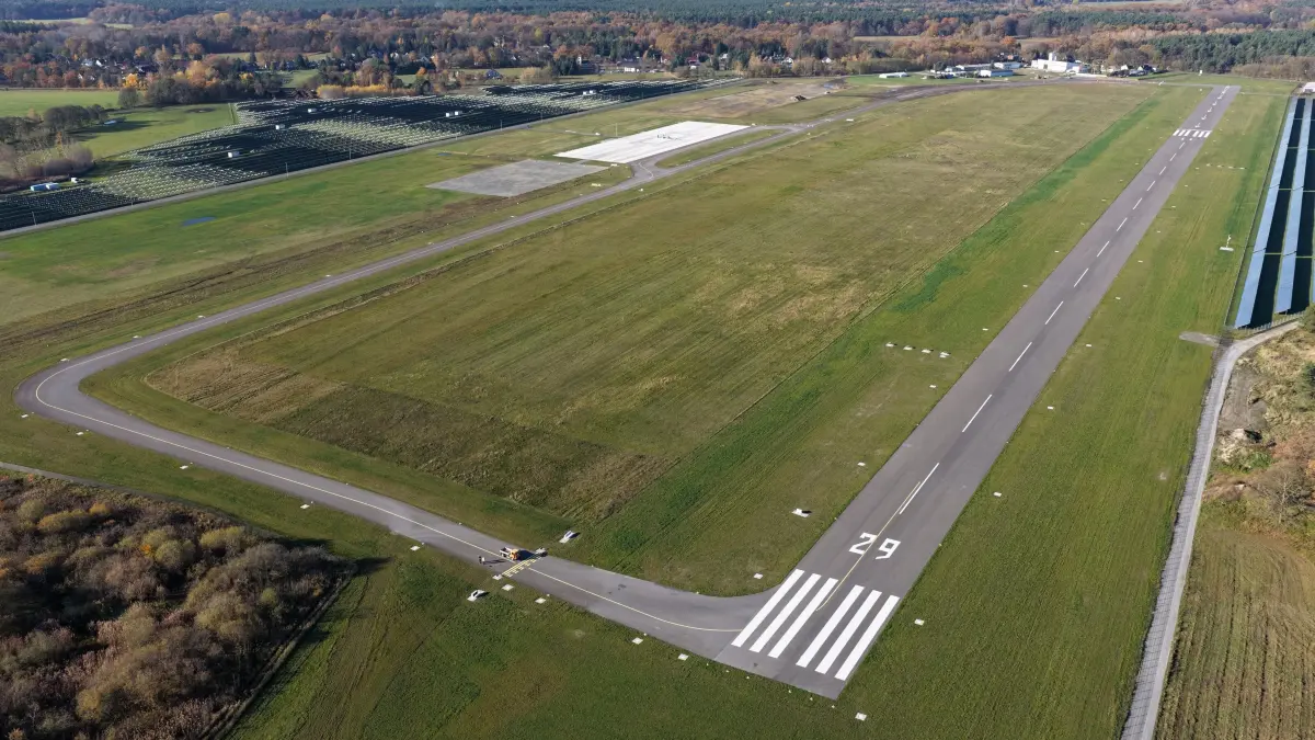 Flugplatz Neuhausen Einweihung: Blick auf die asphaltierte Start- und Landebahn (rechts) sowie die asphaltierte Rollbahn (links) mit dem Flugvorfeld mit Tankstelle für Flugbenzin.
Luftaufnahme vom 6. November 2025
Die umfangreichen Investitionen auf dem Verkehrslandeplatz Cottbus/Neuhausen sind umgesetzt, und am Donnerstagnachmittag ist er feierlich eingeweiht worden. Dank der umfangreichen Mittel aus dem Strukturwandel-Fonds des Bundeslandes Brandenburg, rund 9,6 Millionen Euro Strukturstärkungsmittel, (Gesamtkosten 10,75 Millionen Euro) wurden eine asphaltierte Start- und Landebahn (1080m x 23m) geschaffen, um eine ganzjährige witterungsunabhängige Nutzung zu ermöglichen, das Vorfeld befestigt, neue Rollwege für Flugzeuge sind entstanden, und eine neue Tankstelle für Flugzeugbenzin steht zur Verfügung. Der Flugplatz soll künftig enger Kooperationspartner des Deutschen Zentrums für Luft- und Raumfahrt (DLR) mit seinen Cottbuser Instituten für CO2-arme Industrieprozesse und Elektrifizierte Luftfahrtantriebe sowie der Brandenburgischen Technischen Universität Cottbus-Senftenberg (BTU) sein.