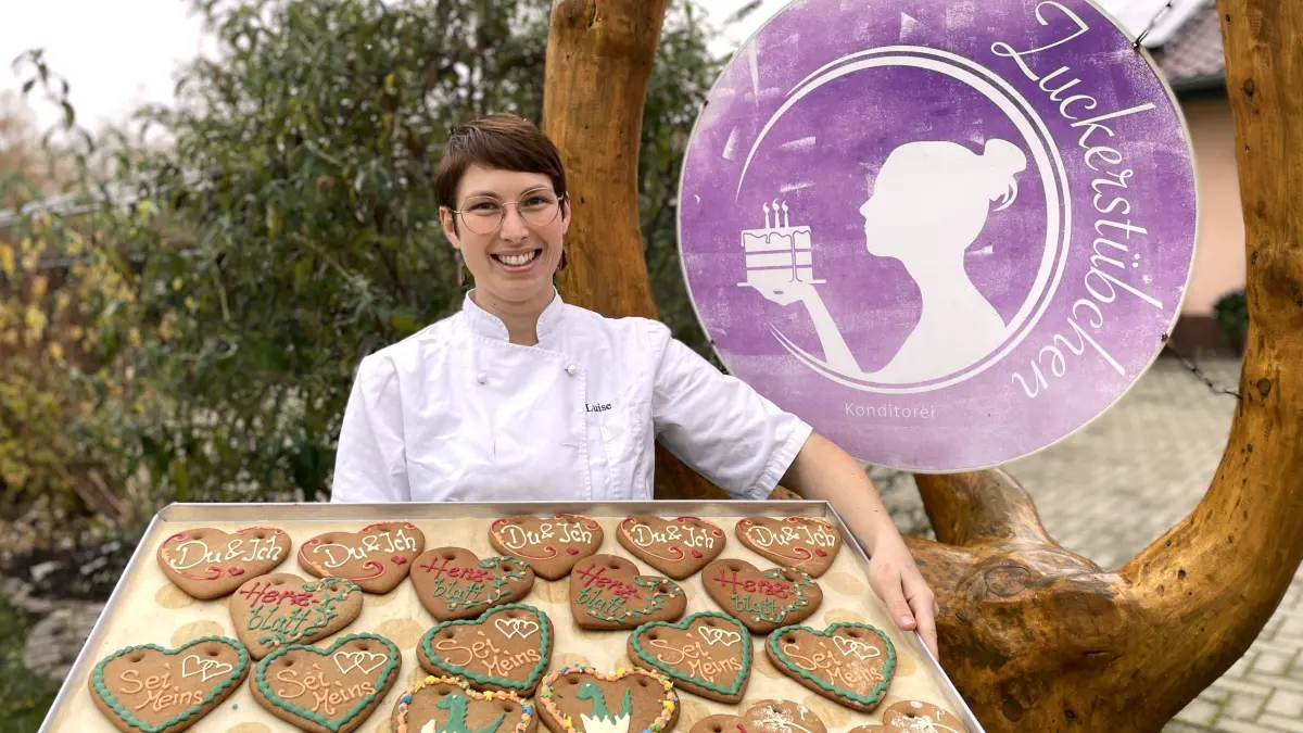 Luise Wille, Chefin der Konditorei Zuckerstübchen, posiert mit Lebkuchenherzen vor ihrem Geschäftsschild in Kasel-Golzig am 11. 11. 2025.