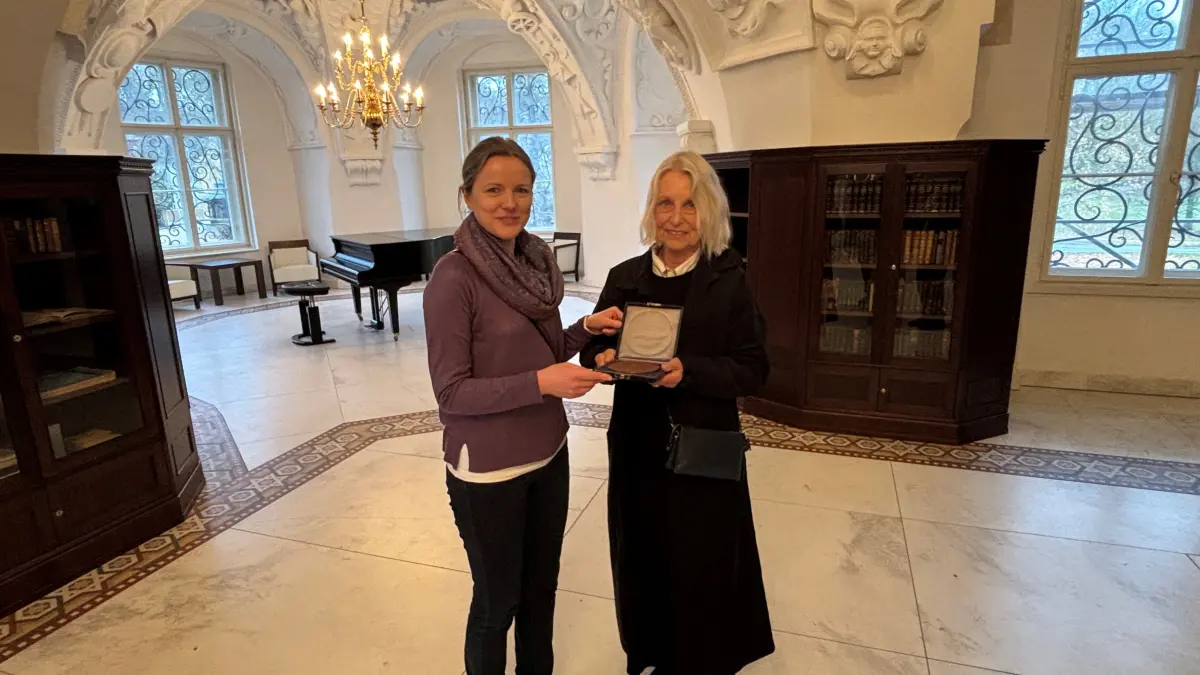Madeleine Anders-McLendon (rechts) übergibt Stefanie Fink, die bei der Fürst-Pückler-Stiftung die Abteilungen Kunstgeschichte, Kultur und Besucherservice leitet, in der Bibliothek im Muskauer Schloss ein ganz besonderes Geschenk von ihrem Urgroßvater.