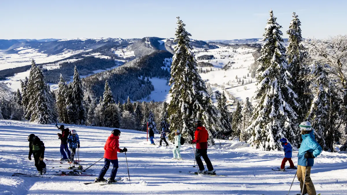 Bei blauem Himmel und Sonnenschein fahren Skifahrer auf einer Skipiste.