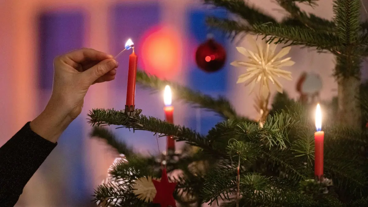 Weihnachtsbaum: ARCHIV - 24.12.2022, Baden-Württemberg, Stuttgart: Eine Frau zündet eine Kerze an einem Weihnachtsbaum an. (zu dpa: «Weihnachtsbaum aus der Region – worauf Käufer achten sollten») Foto: Marijan Murat/dpa +++ dpa-Bildfunk +++