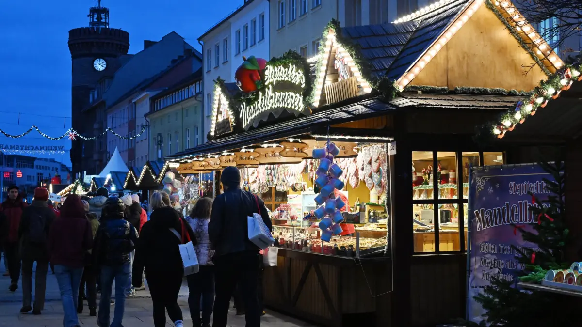 Weihnachtsmarkt 2025 Abend: Blick auf den abendlichen Cottbuser Weihnachtsmarkt der 1000 Sterne. Täglich lädt er von 11 bis 19 Uhr zum Bummeln und Verweilen ein. Er endet auf dem Altmarkt am 28. Dezember 2025. Tags zuvor, am 27.Dezember, gibt es auf dem Altmarkt den traditionellen Rückkehrertag. Die Marktteile in der Spremberger Strasse sowie am Platz am Stadtbrunnen enden bereits am 23. Dezember 2025. Die Gastronomie öffnet bis 21.00 Uhr. In diesem Jahr sind rund 90 Händler bzw. Teilnehmer vertreten. Dazu zählen auch 15 Glühweinstände.
Ein besonderes Highlight ist in diesem Jahr die Rückkehr einer echten Eisbahn. Das erste Mal seit vielen Jahren gibt es wieder eine echte Eisbahn mit richtigem Eis statt Kunststoff zum Schlittschuhlaufen. Die Bahn 29,5 mal 12 Meter große Bahn befindet sich am Postparkplatz in der Stadtpromenade zwischen Eventfläche und Flaniermeile. Am Rand der Eisbahn können sich die Besucher an Imbiss- und Getränkeständen stärken.