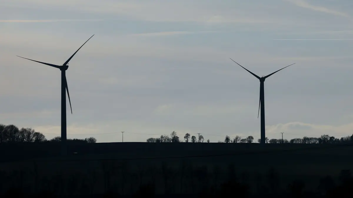 Windräder hinter Dorf: 04.12.2025, Thüringen, Neubraunshain: Mehrere Windkraftanlagen stehen auf einem Kamm. In Thüringen gelten für Windräder seit 2024 Mindestabstände zu Wohngebieten von 1000 Metern. Foto: Jan Woitas/dpa - Honorarfrei nur für Bezieher des Dienstes ZB-Funkregio Ost +++ ZB-FUNKREGIO OST +++