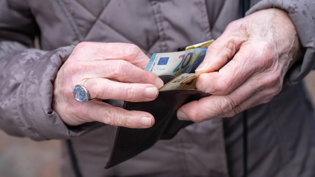 Senioren: 02.12.2025, Bremen: Die Hände einer älteren Person halten eine geöffnete Geldbörse, aus der ein 20-Euro-Schein hervorragt. Im Bundestag steht am Freitag die Entscheidung über die geplante Rentenreform an, die ein stabiles Rentenniveau, erweiterte Kindererziehungszeiten, steuerfreie Zuverdienstmöglichkeiten im Alter und weitere Änderungen in der Altersvorsorge vorsieht. (zu dpa: «Rentenpaket: Mehr Geld für Rentner, Mütter, Senioren im Job») Foto: Sina Schuldt/dpa +++ dpa-Bildfunk +++