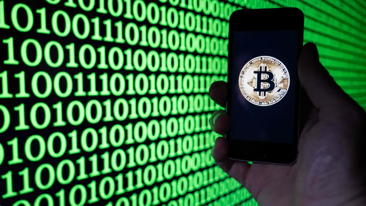This illustration photograph shows a man holding a phone displaying a Bitcoin logo, in Mulhouse on December 5, 2025. (Photo by SEBASTIEN BOZON / AFP)