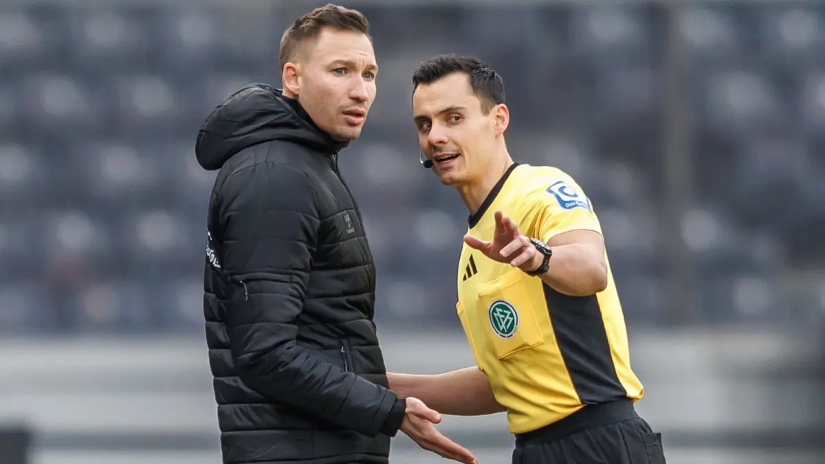 Hertha BSC - 1. FC Magdeburg: 07.12.2025, Berlin: Fußball, 2. Bundesliga, Hertha BSC - 1. FC Magdeburg, 15. Spieltag, Olympiastadion. Schiedsrichter Konrad Oldhafer (r) bespricht sich mit Pascal Ibold, einer der beiden Trainer des 1. FC Magdeburg. Foto: Andreas Gora/dpa - WICHTIGER HINWEIS: Gemäß den Vorgaben der DFL Deutsche Fußball Liga bzw. des DFB Deutscher Fußball-Bund ist es untersagt, in dem Stadion und/oder vom Spiel angefertigte Fotoaufnahmen in Form von Sequenzbildern und/oder videoähnlichen Fotostrecken zu verwerten bzw. verwerten zu lassen. +++ dpa-Bildfunk +++