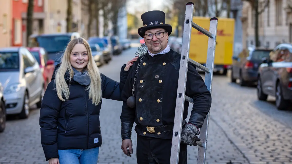 Schornsteinfeger sind Glücksbringer: Lisa Rademacher greift Schornsteinfeger Torsten Wende an seine rechte Schulter. Das Berühren eines Schornsteinfegers soll Glück bringen. Besonders zum Jahreswechsel wird die Rolle als Glücksbringer betont.