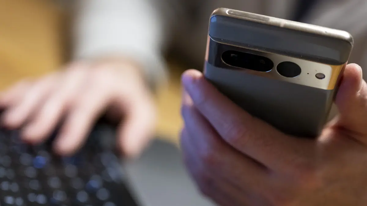 Eine Person sitzt am Laptop und hält ein Smartphone mit in der Hand. (zu dpa: «Frau verliert 100.000 Euro durch Online-Betrug») +++ dpa-Bildfunk +++
