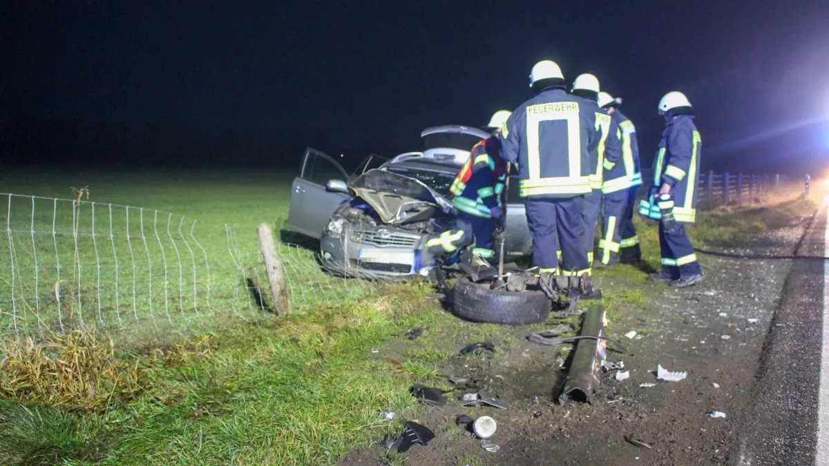 Unfall bei Neuhausen: Einsatzkräfte der Feuerwehr an dem Pkw, der beim Aufprall auf ein Feld neben der Straße geschleudert wurde. Auf der Fahrbahn liegen Trümmerteile von der Kollision.