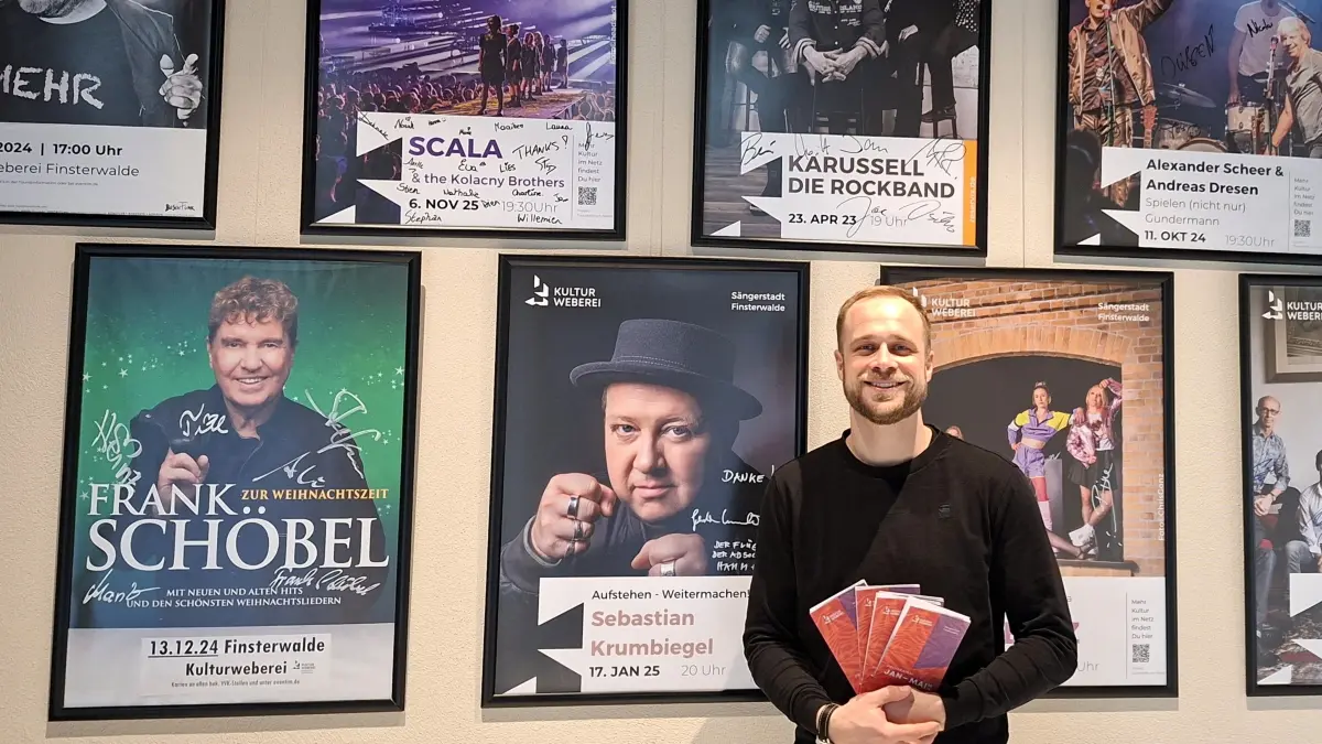 Jonas Gallin, Eventmanager in der Kulturweberei Finsterwalde, vor einer der Wände, wo Künstler sich auf den Veranstaltungsplakaten verewigt haben.