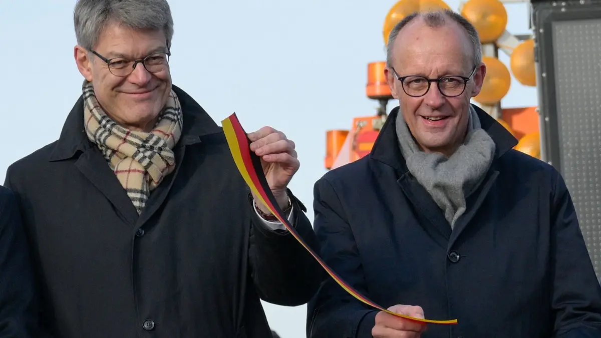German Transport Minister Patrick Schnieder (L) and German Chancellor Friedrich Merz after cutting the ribbon at the opening ceremony for the reconstructed Rahmede bridge on the A45 motorway, near Luedenscheid, western Germany on December 22, 2025. Following a routine inspection of the Rahmede viaduct in December 2021, inspectors discovered deformations in the steel wall that could affect the bridge's load-bearing capacity, leading to its reconstruction. (Photo by Sascha Schuermann / AFP)