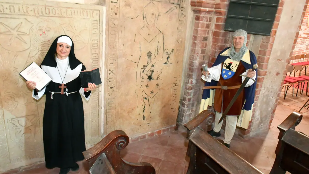 Ein alter Stein in der Klosterkirche Mühlberg zeigt einen Ritter mit Fähnchen, Schwert sowie mit einem Schild. darauf sind ein Löwe und drei Sterne zu sehen. Es ist das Wappen der Ileburger. Passend dazu haben sich Diana und Jens Uhlemann aus Winkel als Nonne der Zisterzienser sowie als Ritter der Ileburger kostümiert. Vorlage für den Ritter war der über 700 Jahre alte Stein in der Klosterkirche.