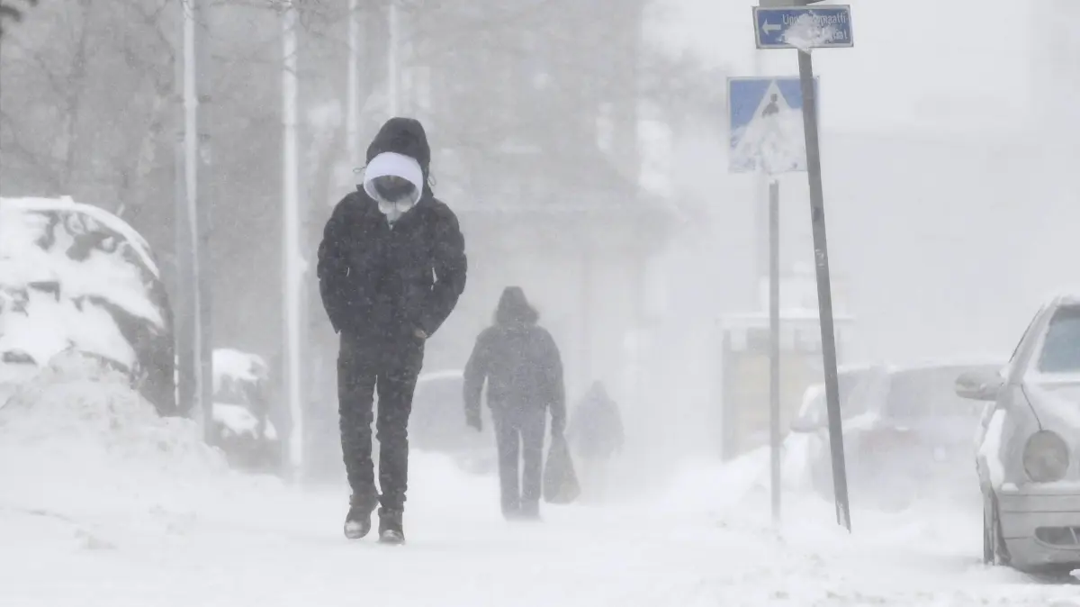 Zwei Passanten gehen über einen verschneiten Gehweg. Schneechaos, heftiger Wind und heranziehende Eiseskälte haben in Teilen Skandinaviens Stromausfälle, Verkehrsbehinderungen und weitere Probleme verursacht. +++ dpa-Bildfunk +++