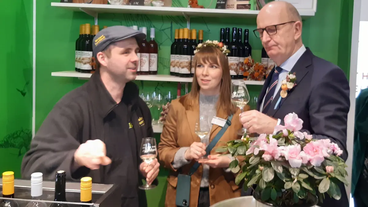 Das Weingut von Rico Leonhardt (l.) präsentiert am Elbe-Elster-Stand die regional erzeugten Weine. Ministerpräsident Dietmar Woidke hat am Brandenburgtag verkostet und Tina Faber von der Tourismusförderung im Kreisentwicklungsamt (Mitte) hat den Regierungschef mit Elbe-Elsters Blütenkranz ausgestattet.