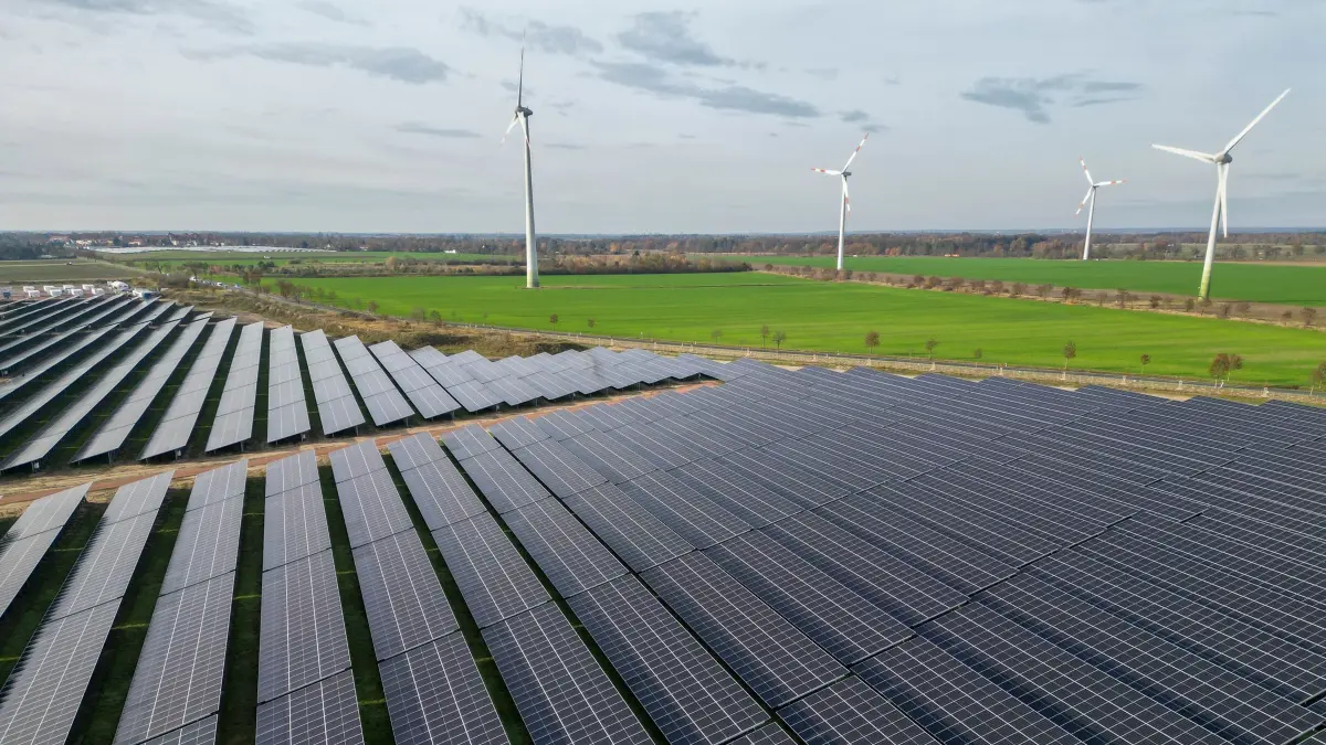 Windräder hinter Solarpark: ARCHIV - 12.11.2025, Sachsen-Anhalt, Zerbst: Windkraftanlagen drehen sich hinter den Solaranlagen eines neuen PV-Batteriespeicher-Hybridkraftwerk. (Luftaufnahme mit Drohne) (zu dpa: «Mehr Strom in EU aus Wind und Solar als aus fossiler Energie») Foto: Jan Woitas/dpa +++ dpa-Bildfunk +++