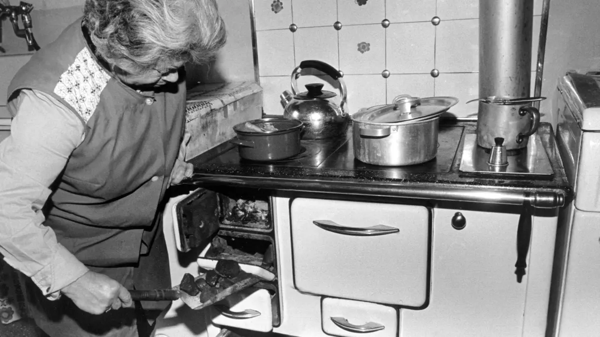 ARCHIV - Eine Hausfrau schiebt mit einer Schaufel neue Kohle in ihren alten Ofen nach, aufgenommen am 17. April 1979 in München. Foto: Ludwig Hamberger dpa (zu dpa-Serie Deutsche Geschichte - Deutsche Geschichten vom 16.06.) nur s/w +++ dpa-Bildfunk +++