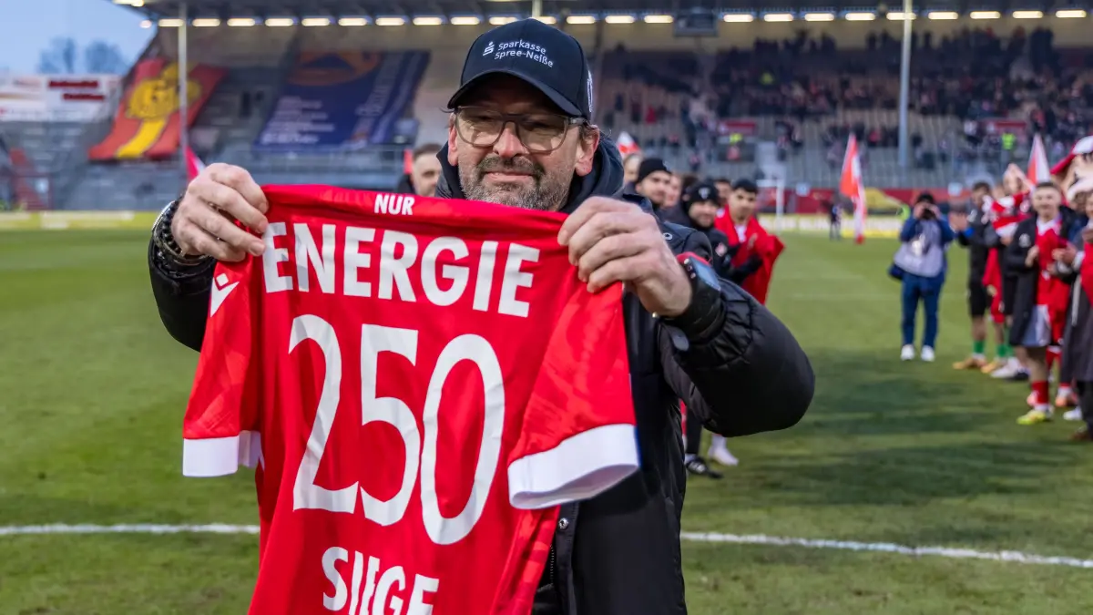 3. Liga Saison 25/26 FC Energie Cottbus vs TSG 1899 Hoffenheim II: Fußball: Dritte Liga, FC Energie Cottbus - VfB Stuttgart II, LEAG Energie Stadion: Cheftrainer Claus-Dieter Wollitz (FC Energie Cottbus) hält ein Trikot mit der Aufschrift «250 Siege Pele Wollitz» in der Hand.