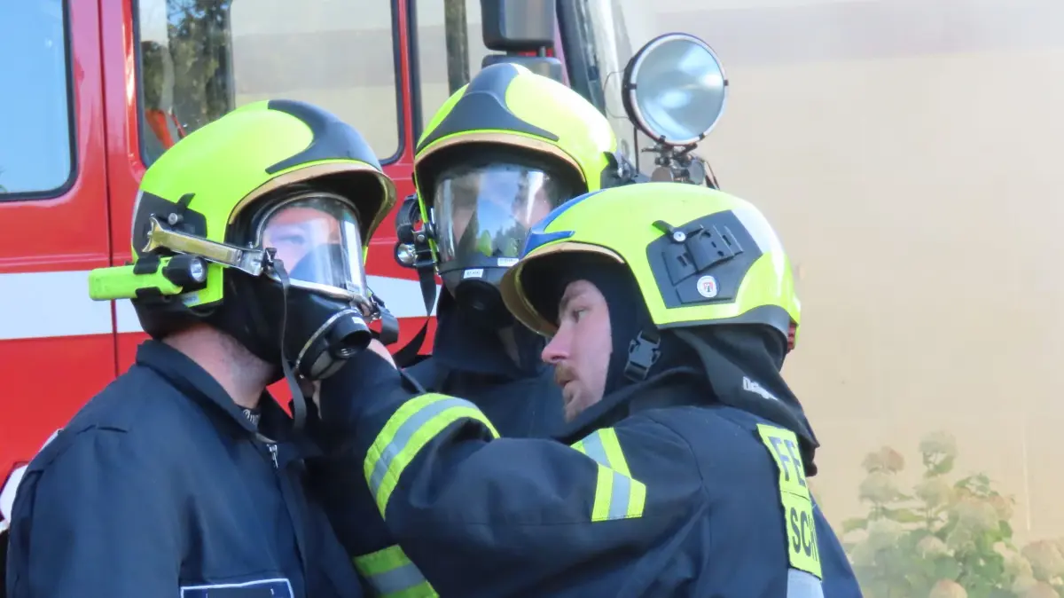 Feuerwehrleute helfen sich vor ihrem Einsatz 2024 in Welzow beim Anlegen des Atemschutzgerätes.