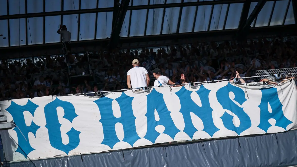 Fans des FC Hansa Rostock: ARCHIV - 16.08.2025, Mecklenburg-Vorpommern, Rostock: Fußball: DFB-Pokal, Hansa Rostock - TSG 1899 Hoffenheim, 1. Runde, Ostseestadion, Fans von Hansa Rostock mit Banner im Spiel. (zu dpa: «Fan-Gewalt: Polizei-Gewerkschaft warnt vor Rostock-Aufstieg») Foto: Christian Charisius/dpa - WICHTIGER HINWEIS: Gemäß den Vorgaben der DFL Deutsche Fußball Liga bzw. des DFB Deutscher Fußball-Bund ist es untersagt, in dem Stadion und/oder vom Spiel angefertigte Fotoaufnahmen in Form von Sequenzbildern und/oder videoähnlichen Fotostrecken zu verwerten bzw. verwerten zu lassen. +++ dpa-Bildfunk +++