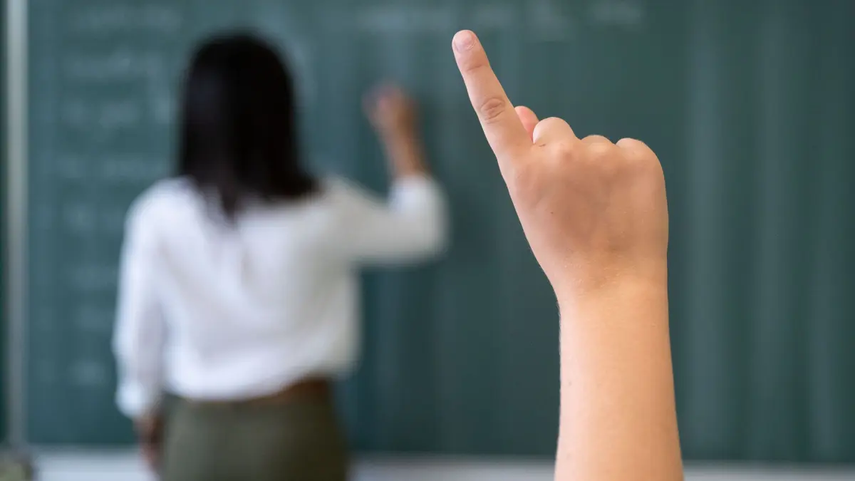 Unterricht in der Schule: ARCHIV - 08.07.2020, Baden-Württemberg, Marbach am Neckar: Ein Schüler meldet sich während einer Unterrichtsstunde in einem Gymnasium, während eine Lehrerin an die Tafel schreibt. (zu dpa: «Zahl der Schulbegleiter wächst rasant») Foto: Marijan Murat/dpa +++ dpa-Bildfunk +++