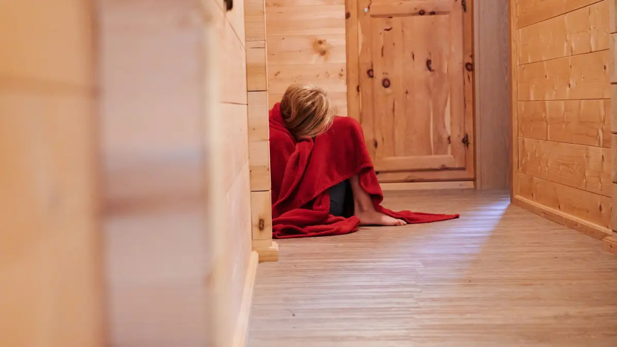 Illustration - Gewalt an Kindern: ARCHIV - 01.08.2022, Österreich, Mayrhofen: Ein Kind ist in eine Decke gewickelt und kauert auf dem Boden eines Hausflures (gestellte Szene). (zu dpa: «Uni untersucht möglichen Missbrauch im fränkischen Heim») Foto: Annette Riedl/dpa +++ dpa-Bildfunk +++