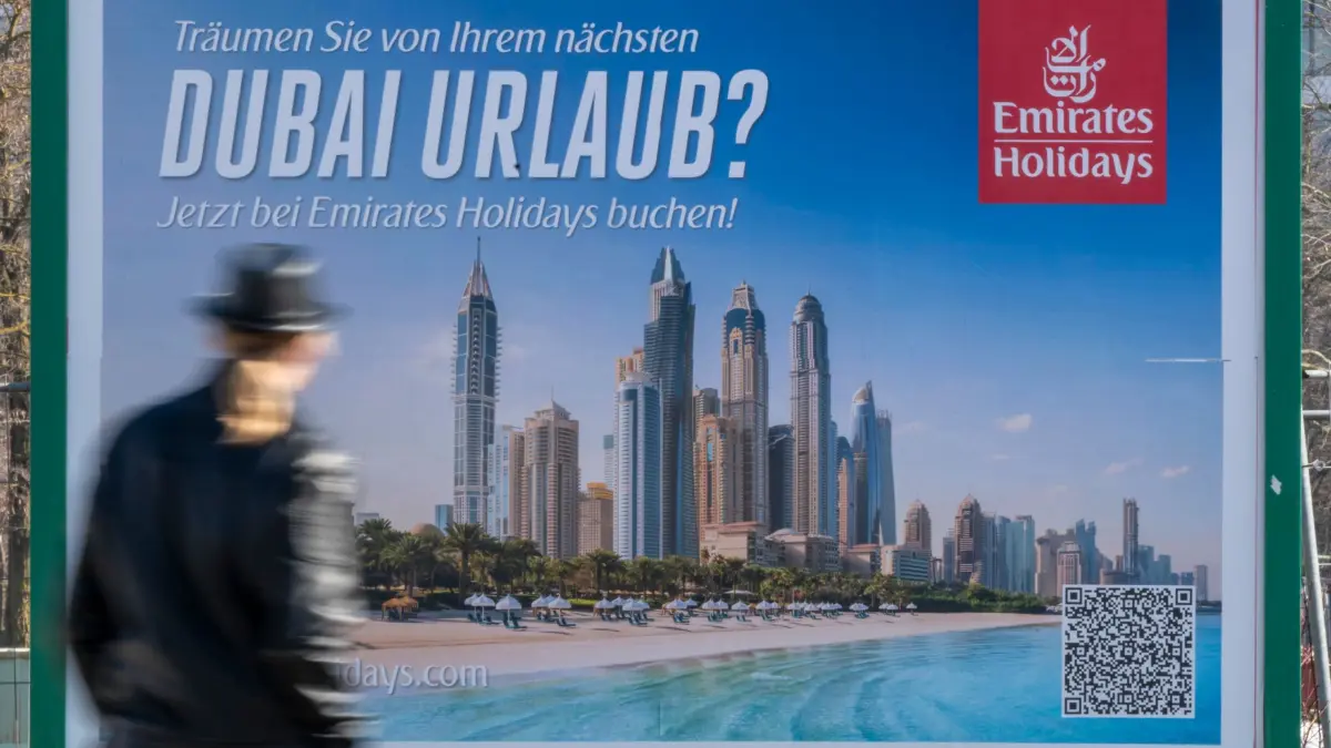 Iran-Krieg - Dubai-Werbung in München: 05.03.2026, Bayern, München: Ein Mann geht an einem Plakat mit der Aufschrift «Träumen sie von Ihrem nächsten Dubai Urlaub? - Jetzt bei Emirates Holidays buchen!» vorbei, das großflächig am Strasserand im Norden der bayerischen Landeshauptstadt hängt. Foto: Peter Kneffel/dpa - ACHTUNG: Nur zur redaktionellen Verwendung im Zusammenhang mit der aktuellen Berichterstattung und nur mit vollständiger Nennung des vorstehenden Credits +++ dpa-Bildfunk +++