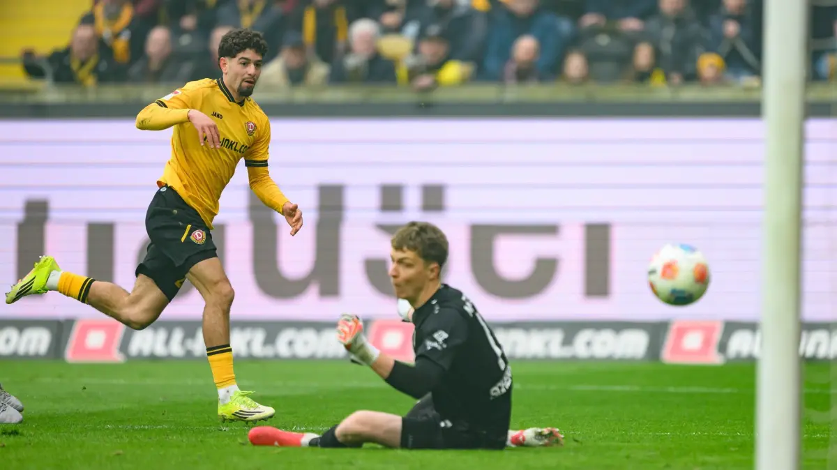 SG Dynamo Dresden - Preußen Münster: 15.03.2026, Sachsen, Dresden: Fußball, Männer: 2. Bundesliga, SG Dynamo Dresden - Preußen Münster, 26. Spieltag, Rudolf-Harbig-Stadion, Ben Bobzien (Dynamo Dresden, l) erzielt gegen Johannes Schenk (Preußen Münster) das Tor zum 1:0. Foto: Robert Michael/dpa - WICHTIGER HINWEIS: Gemäß den Vorgaben der DFL Deutsche Fußball Liga bzw. des DFB Deutscher Fußball-Bund ist es untersagt, in dem Stadion und/oder vom Spiel angefertigte Fotoaufnahmen in Form von Sequenzbildern und/oder videoähnlichen Fotostrecken zu verwerten bzw. verwerten zu lassen. +++ dpa-Bildfunk +++