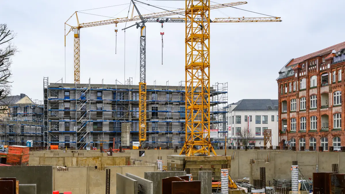 Auf einer Baustelle für sozialen Wohnungsbau stehen mehrere Baukräne und Rohbauten.