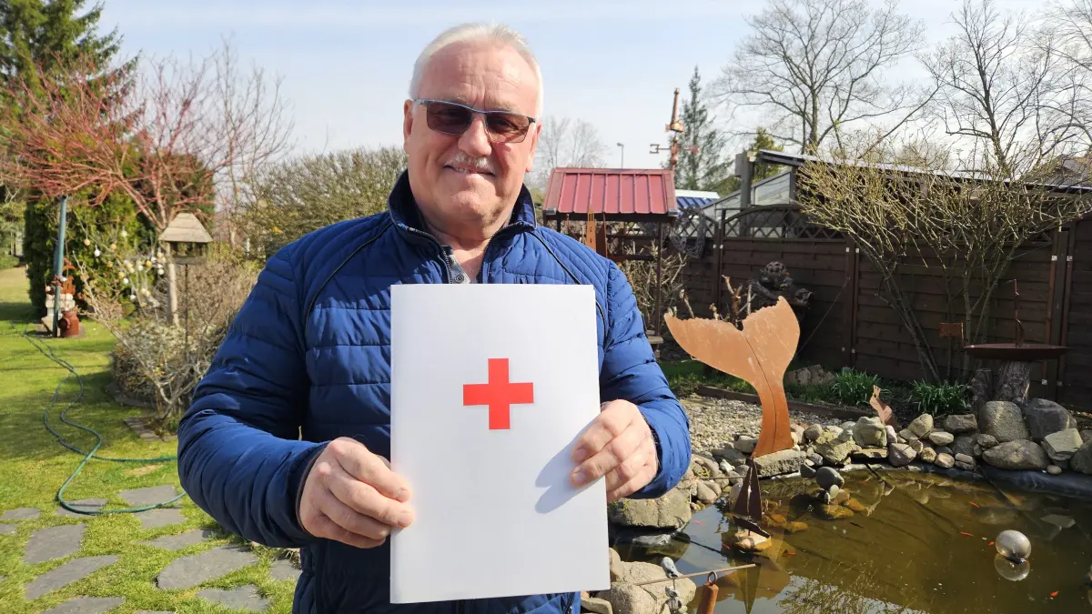 Frank Jentsch (67) aus Lauchhammer in seinem Garten. In den Händen hält er eine DRK-Mappe mit der Urkunde zu seinem 150. Spendenjubiläum – eine der letzten Auszeichnungen, die er für sein langjähriges Engagement erhielt.
