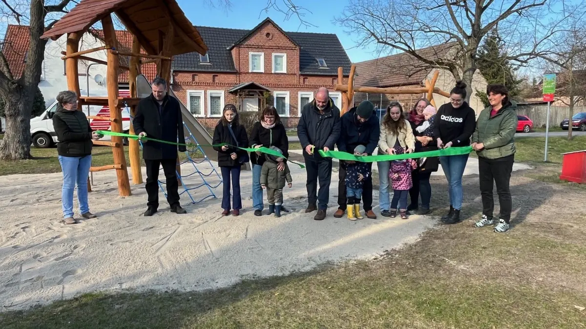 Bürgermeister Michael Stawski (Mitte) und Bauamts- und Ordnungsleiter Christoph Schulze (2. v. l.) durchtrennen gemeinsam mit Bewohnern und Kindern das Band zur Einweihung des neuen Spielplatzes in Brandis.