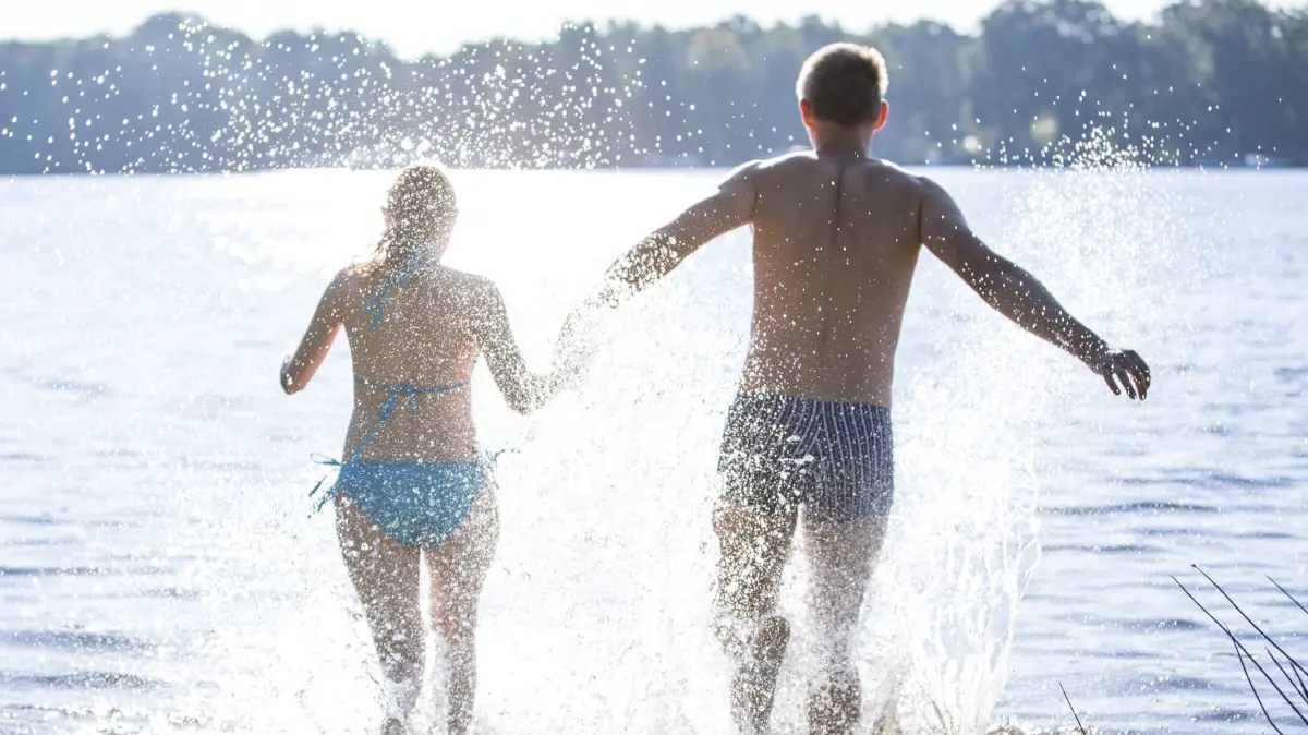 Paar geht in einem See baden: ILLUSTRATION - Einfach so in den See springen? Ist dieser von öffentlichem Gelände aus erreichbar, ist das in der Regel unproblematisch. (zu dpa: «Grillen, Baden, Feiern: Was verträgt sich mit dem Gesetz?») Foto: Christin Klose/dpa-tmn - Honorarfrei nur für Bezieher des dpa-Themendienstes +++ dpa-Themendienst +++