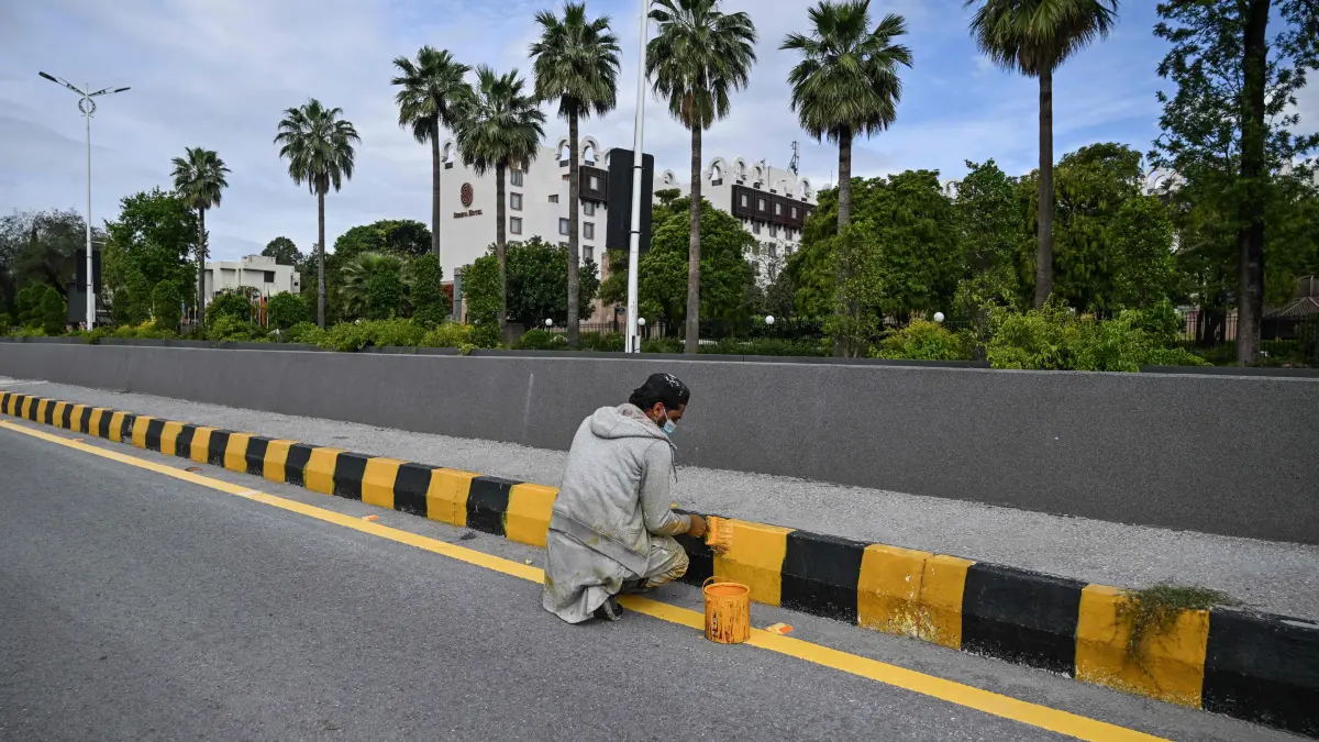 A worker paints a road separator near the Serena Hotel, the expected venue for US–Iran talks, in the Red Zone area of Islamabad on April 9, 2026. An Iranian delegation is expected to arrive in Islamabad late on April 9 ahead of Pakistan-brokered talks with the United States, Iran's envoy said. Pakistan has been preparing for talks involving representatives from the US and Iran over the Mideast war, with the White House saying Vice President JD Vance would lead negotiations in Islamabad "this weekend". (Photo by Aamir QURESHI / AFP)