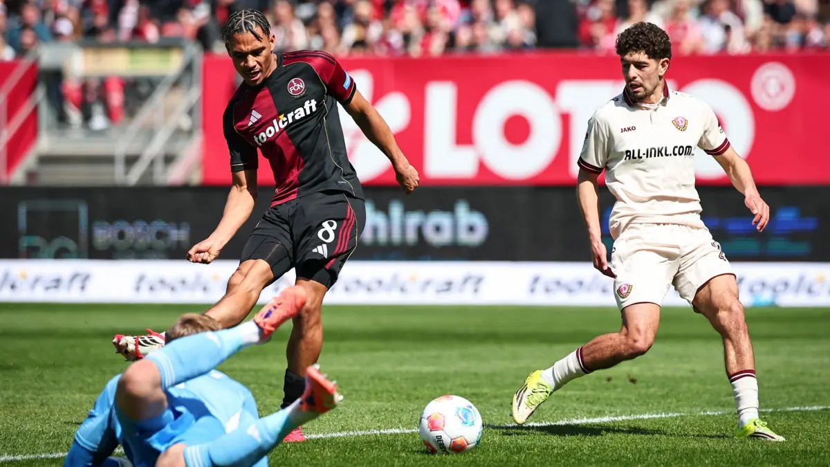 1. FC Nürnberg - Dynamo Dresden: 11.04.2026, Bayern, Nürnberg: Fußball, Männer: 2. Bundesliga, 1. FC Nürnberg - Dynamo Dresden, 29. Spieltag im Max-Morlock-Stadion. Henri Koudossou (M, 1. FC Nürnberg) schießt versehentlich den Ball ins eigene Tor zum anschließenden 0:1 für Dresden. Unten ist sein Kollege Jan Reichert (1. FC Nürnberg) und links Ben Bobzien (Dynamo Dresden). Foto: Daniel Karmann/dpa - WICHTIGER HINWEIS: Gemäß den Vorgaben der DFL Deutsche Fußball Liga bzw. des DFB Deutscher Fußball-Bund ist es untersagt, in dem Stadion und/oder vom Spiel angefertigte Fotoaufnahmen in Form von Sequenzbildern und/oder videoähnlichen Fotostrecken zu verwerten bzw. verwerten zu lassen. +++ dpa-Bildfunk +++