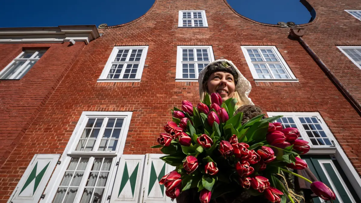 Potsdamer Tulpenfest: ARCHIV - 09.04.2025, Brandenburg, Potsdam: Friederike steht in der historischen Tracht der Niederländerin Jacoba van Beieren mit einem Strauß Tulpen während eines Pressetermins zum bevorstehenden Tulpenfest vor den Häusern des Holländerviertels. Das Tulpenfest findet am 12. und 13.04.2025 statt. (zu dpa: «Tausende Tulpen bringen Brandenburgern Frühlingsgefühle») Foto: Soeren Stache/dpa +++ dpa-Bildfunk +++