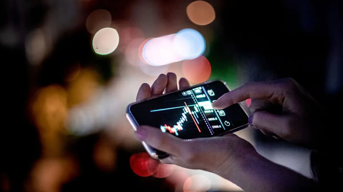 Mann hält ein Smartphone mit einer Trading-App in der Hand: ILLUSTRATION - Wer mit Kryptowährungen handelt, muss die Geschäfte penibel und nachvollziehbar als Nachweis fürs Finanzamt dokumentieren. (zu dpa: «Krypto-Gewinne gemacht? Was Sie jetzt versteuern müssen») Foto: Zacharie Scheurer/dpa-mag - Honorarfrei nur für Bezieher des Dienstes dpa-Magazin +++ dpa-Magazin +++