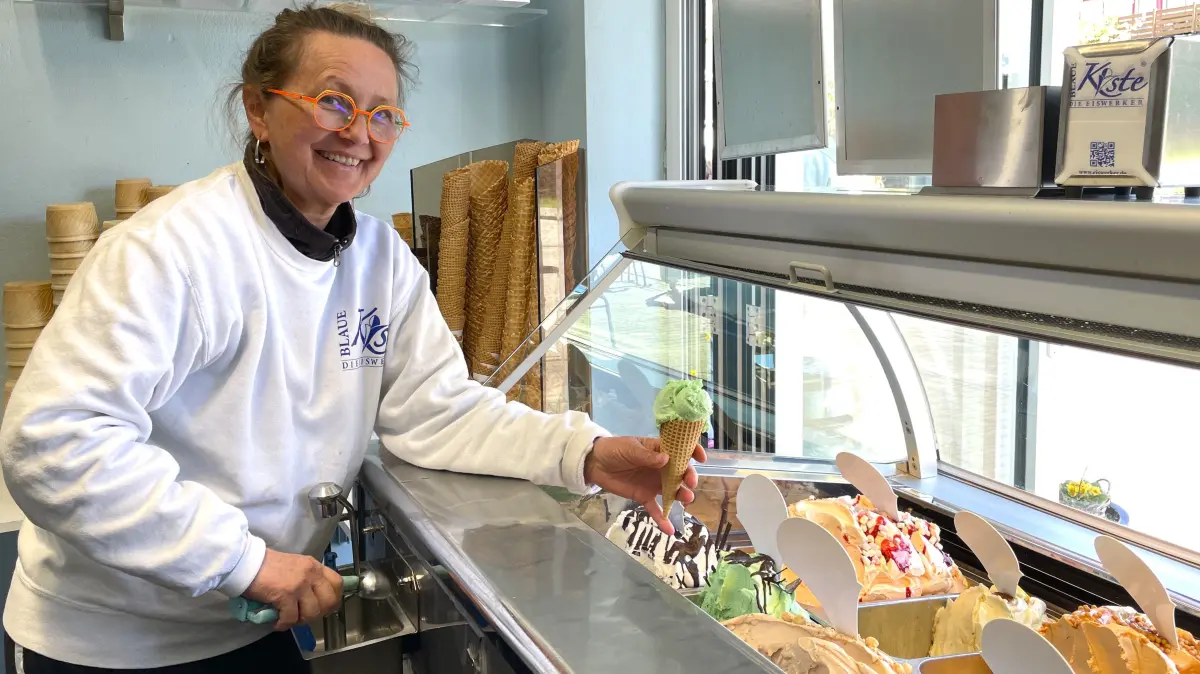 Sylke Buchan-Schulze, Chefin der Eisdiele "Blaue Kiste" in Burg im Spreewald, hält am 22.04.2026 eine Waffel mit einer Kugel Schoko-Minz-Eis in die Kamera.