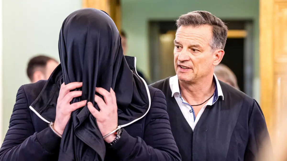 Prozess am Landgericht Cottbus wegen Mordes an Polizisten: 06.05.2026, Brandenburg, Cottbus: Der Angeklagten (l) wird von seinem Verteidiger Christoph Rühlmann in den Verhandlungssaal begleitet. Dem Angeklagten wird Mord an einem 32jährigen Polizisten vorgeworfen. Bei einem Einsatz gegen mutmaßliche Autodiebe vor einem Jahr in Lauchhammer war dieser von einem Fahrzeug erfasst worden und noch am Einsatzort gestorben. Foto: Frank Hammerschmidt/dpa +++ dpa-Bildfunk +++