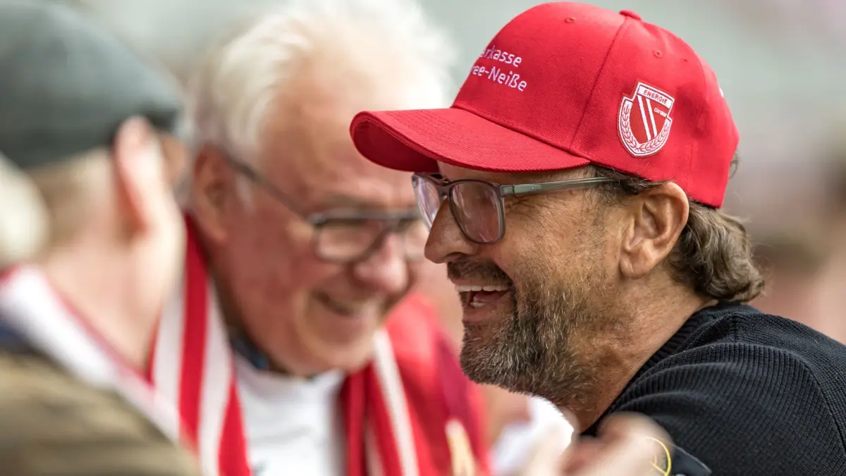 Energie Cottbus - SV Wehen Wiesbaden: 09.05.2026, Brandenburg, Cottbus: Fußball, Männer: 3. Liga, Energie Cottbus - SV Wehen Wiesbaden, 37. Spieltag, LEAG Energie Stadion. Trainer Claus-Dieter Wollitz (FC Energie Cottbus, r) kommt ins Stadion und begrüßt Fans. Foto: Frank Hammerschmidt/dpa +++ dpa-Bildfunk +++