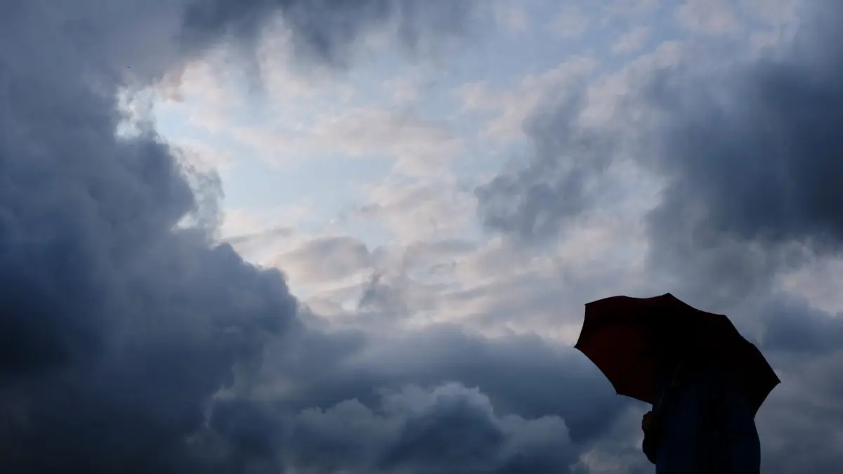 ARCHIV - 12.07.2019, Nordrhein-Westfalen, Duisburg: Ein Mann geht mit einem Regenschirm vor aufziehenden dunklen Wolken spazieren. (zu dpa: «Das Wetter in Nordrhein-Westfalen bleibt wechselhaft») Foto: Martin Gerten/dpa +++ dpa-Bildfunk +++