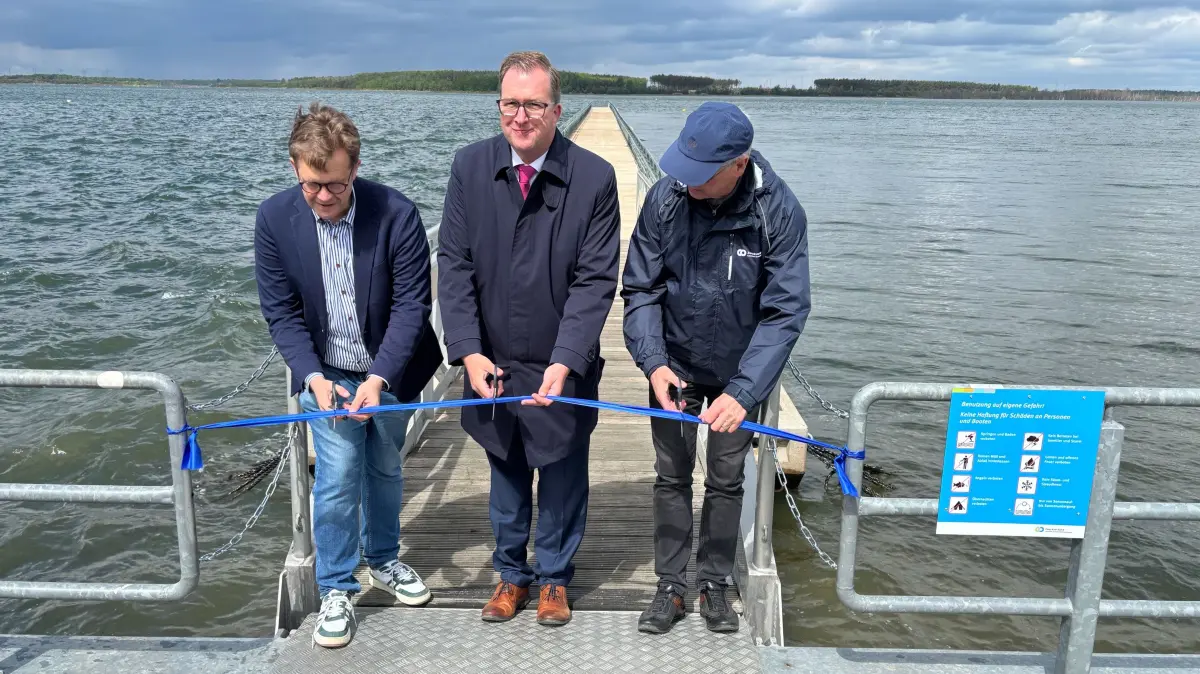 Wiedereinweihung des schwimmenden Steges nach fünf Jahren Abstinenz: Der Senftenberger Bürgermeister Andreas Pfeiffer, Landrat Alexander Erbert und Seenland-Verbandsvorsteher Detlev Wurzler (v.l.) zerschneiden das symbolische blaue Band.
