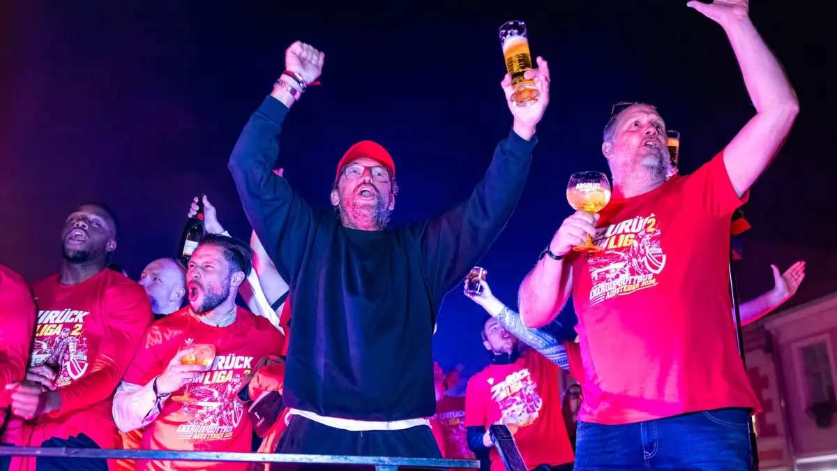 Energie Cottbus ist in der 2. Bundesliga: 17.05.2026, Brandenburg, Cottbus: Die Mannschaft des FC Energie Cottbus, in der Mitte Trainer Claus-Dieter Wollitz, feiert nach ihrer Rückkehr vom letzten Saisonspiel auf dem Cottbuser Altmarkt. Zahlreiche Fans erwarten sie dort. Am Sonntag wird es in der Stadt offizielle Aufstiegsfeierlichkeiten mit Mannschaft und Anhängern geben. Foto: Frank Hammerschmidt/dpa - WICHTIGER HINWEIS: Gemäß den Vorgaben der DFL Deutsche Fußball Liga bzw. des DFB Deutscher Fußball-Bund ist es untersagt, in dem Stadion und/oder vom Spiel angefertigte Fotoaufnahmen in Form von Sequenzbildern und/oder videoähnlichen Fotostrecken zu verwerten bzw. verwerten zu lassen. +++ dpa-Bildfunk +++