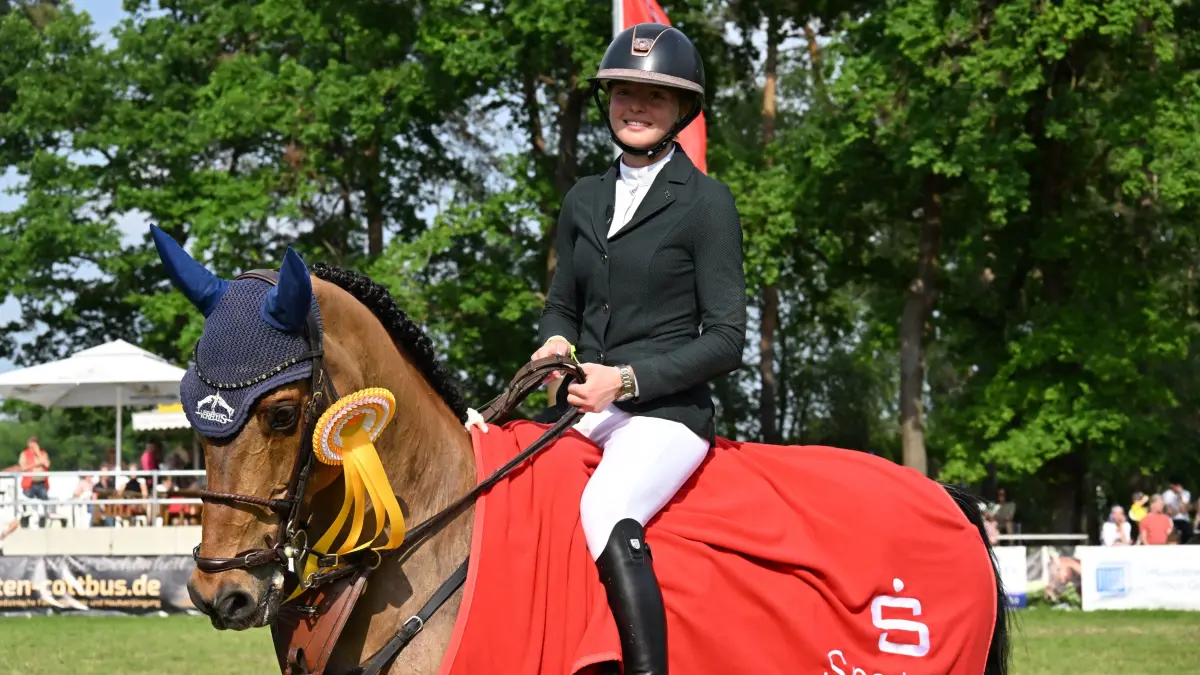 Sielow Reiten Pfingsten 2026: Glückwünsche für Johanna Zander-Keil von der TSG Ponnyfarm Berlin Kladow e.V. und ihr Pferd Boleybawn Actor.
Erstklassigen Reitsport gab es am vergangenen Wochenende beim 54. Pfingst- Reit- und Springturnier des Reitvereins Sielow im Reitstadion Sielow. Rund 700 Nennungen mit 350 Reiter-Pferd-Paaren zu den einzelnen Prüfungen konnten die Veranstalter in diesem Jahr verzeichnen. Auf dem Programm der drei Turniertage standen 21 Springprüfungen, darunter gleich fünf Springen der schweren Klasse. Einer der Höhepunkte war auch in diesem Jahr der mit 6 000 Euro dotierte Große Preis der Sparkasse Spree-Neiße am Pfingstsonntagnachmittag. Die S** Prüfung, die zugleich die Qualifikation für Reiten & Zuchtstartplatz beim CSI in Neustadt/Dosse 2026 war, gewann im Stechen wie im Vorjahr Johanna Zander-Keil von der TSG Ponnyfarm Berlin Kladow e.V. auf Boleybawn Actor in einer Zeit von 41,45 Sekunden und Null Fehlern.