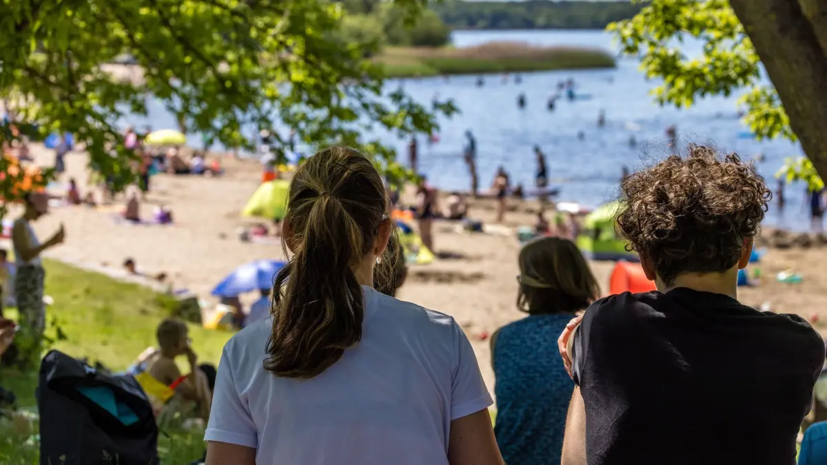 Sommerliches Wetter am Pfingstmontag: 25.05.2026, Brandenburg, Senftenberg: Menschen sitzen im Schatten am Großkoschener Seestrand und schauen zum Uferbereich des Senftenberger Sees. Die Temperaturen in Südbrandenburg werden heute die 30-Grad-Marke nicht erreichen, die Sonne scheint aber ganztägig und es bleibt trocken. Foto: Frank Hammerschmidt/dpa +++ dpa-Bildfunk +++