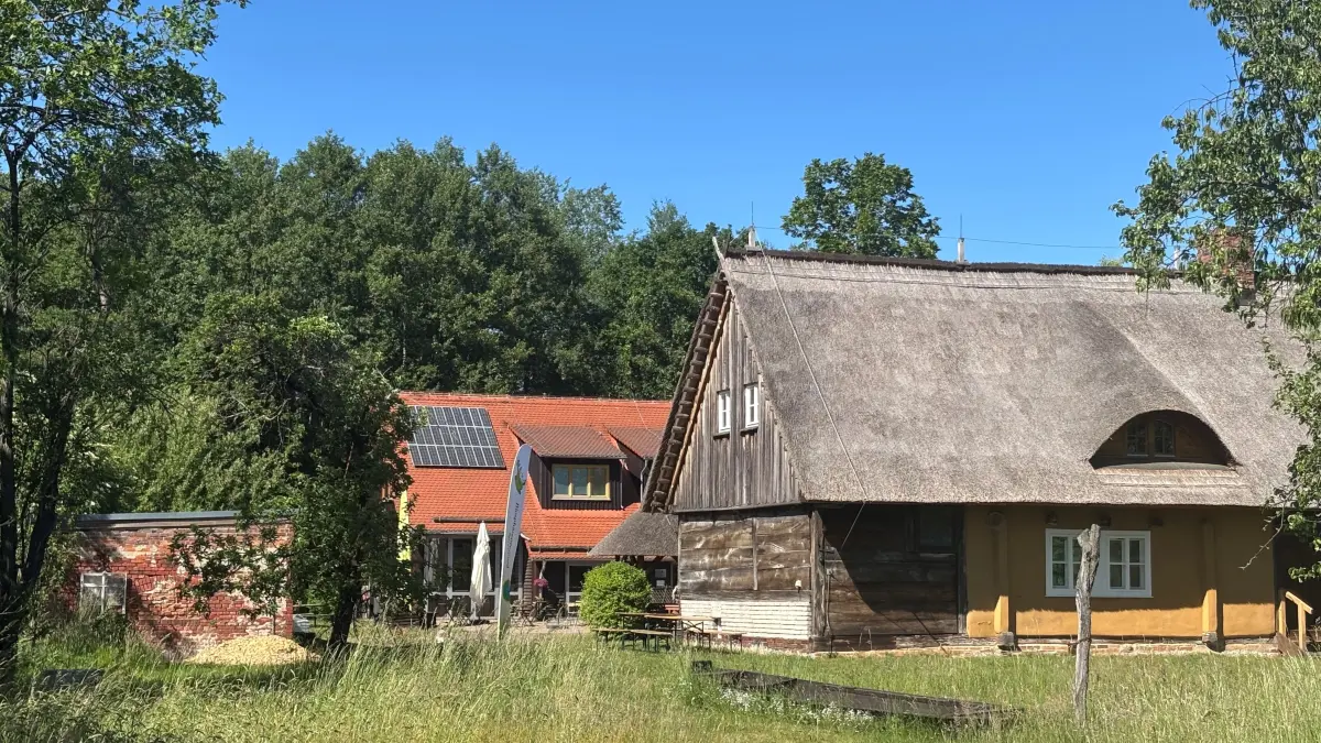 Blick auf das denkmalgeschützte, reetgedeckte Doppelstubenhaus. Links im Bild befinden sich Reste des Scheunenmauerwerks. Am Standort der alten Scheune soll das neue Multifunktionsgebäude errichtet werden.