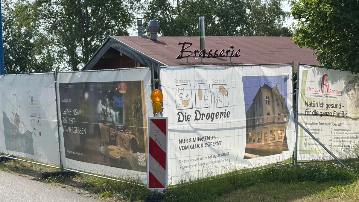 Die Brasserie am Senftenberger See präsentiert sich durch Bauzäune und Banner eingehüllt. Eine Eröffnung im Jahr 2026 wird es nicht geben. Wann dann?