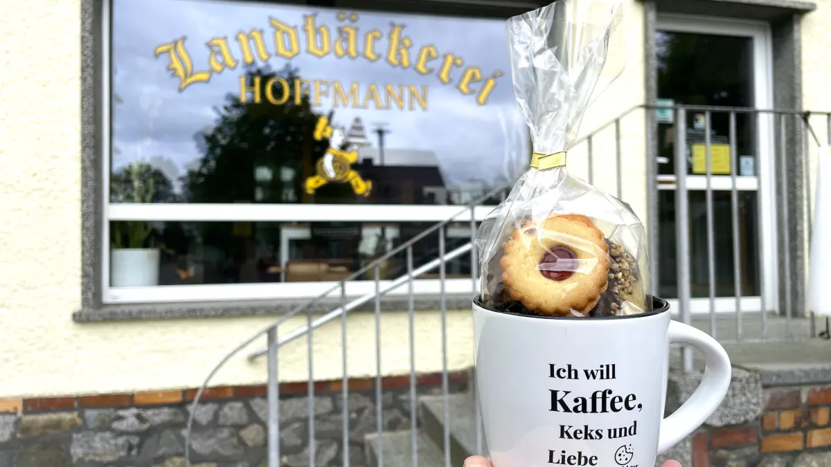 Eine Tasse gefüllt mit Keksen, im Hintergrund das Geschäft der Landbäckerei Hoffmann in Guhrow am 12.05.2026