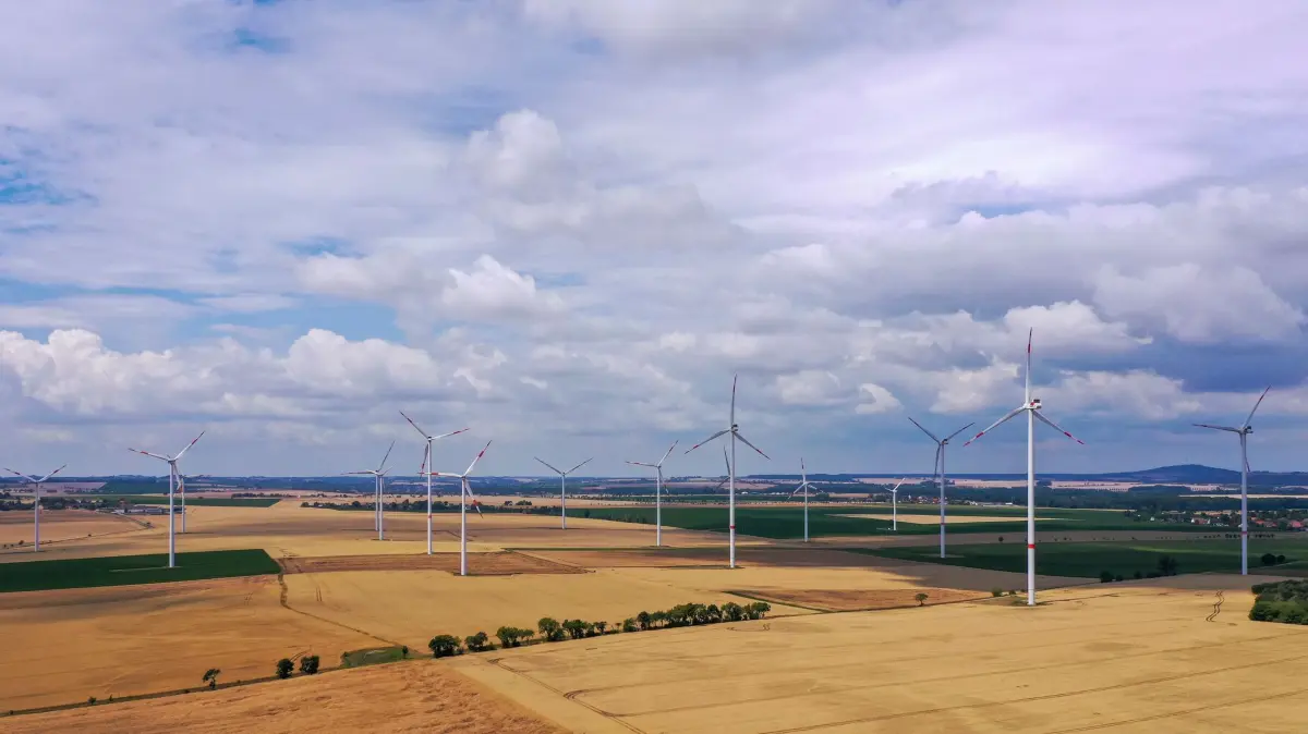 Windkraft in Sachsen: ARCHIV - 17.07.2025, Sachsen, Salbitz: Windräder drehen sich hinter einer Hochspannungsleitung auf einem Feld bei Riesa. (Luftaufnahme mit Drohne) (zu dpa: «Sachsen will bei Windkraftausbau deutlich aufholen») Foto: Jan Woitas/dpa +++ dpa-Bildfunk +++