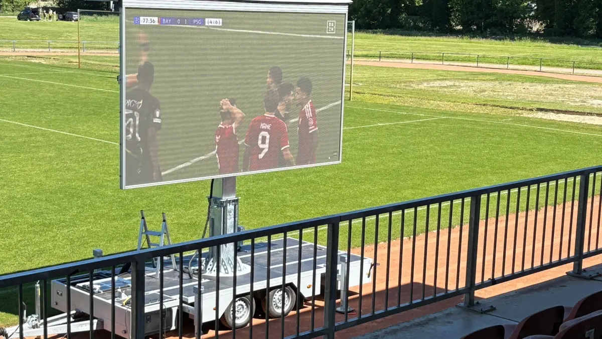 Wettergeschützt auf der Tribüne können Fans in Herzberg die WM‑Spiele auf der aufgebauten Leinwand des Werner-Seelenbinder-Sportplatzes verfolgen.